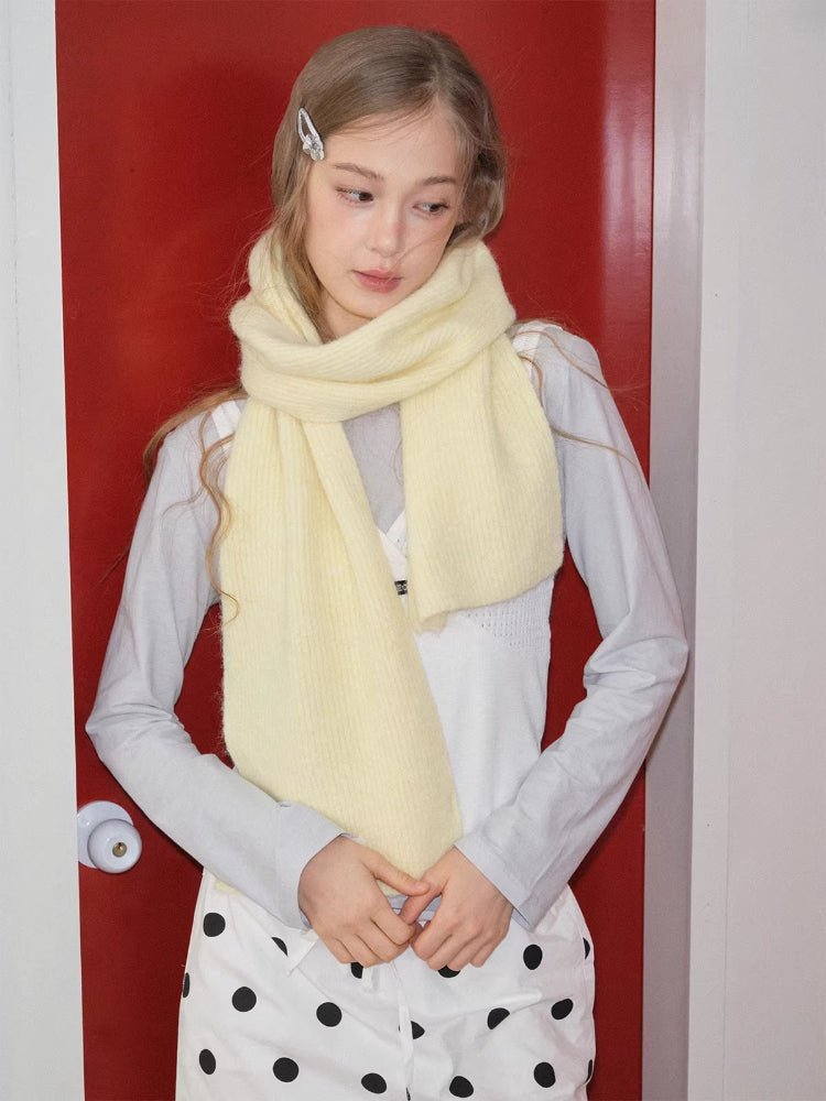 Woman with a pale yellow knit scarf around her neck, looking down.