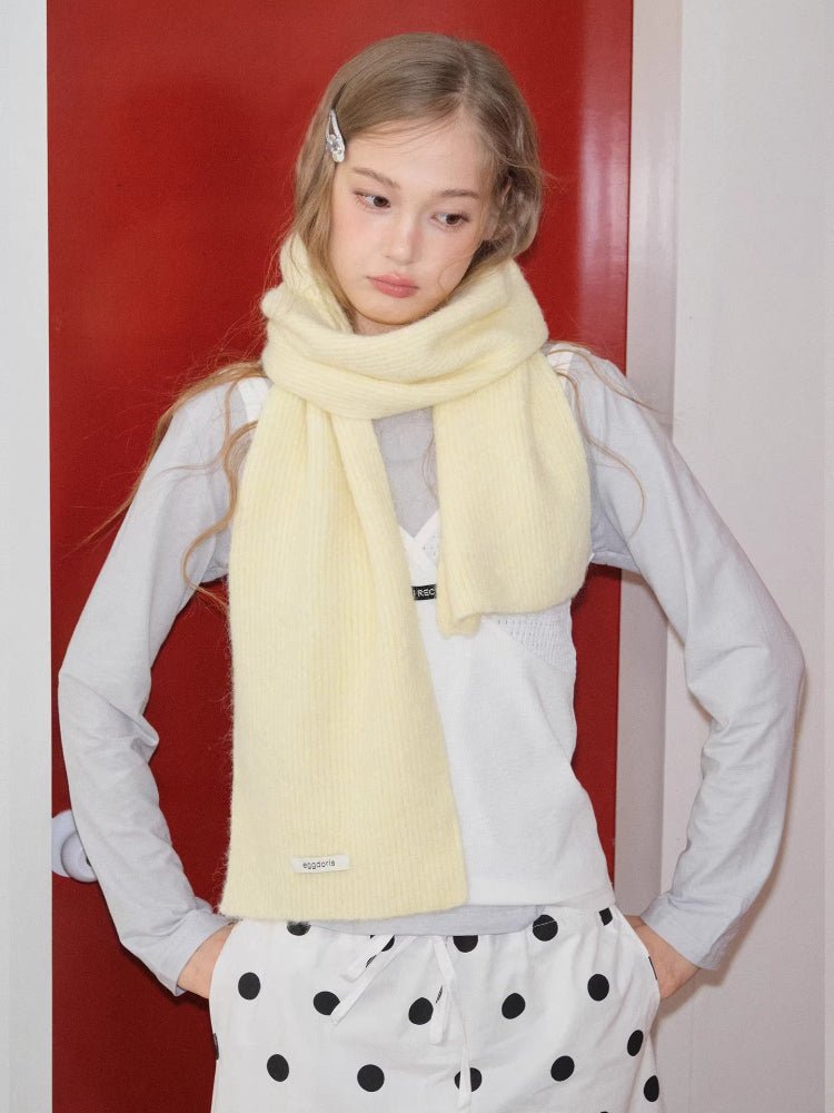 Woman wearing a pale yellow knit scarf wrapped around her neck, standing in front of a red door.