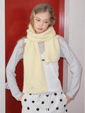 Woman wearing a pale yellow knit scarf wrapped around her neck, standing in front of a red door.