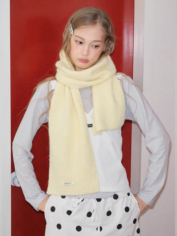 Woman wearing a pale yellow knit scarf wrapped around her neck, standing in front of a red door.