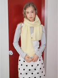 Front view of a woman wearing a pale yellow knit scarf around her neck, hands clasped.