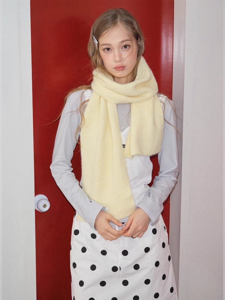 Front view of a woman wearing a pale yellow knit scarf around her neck, hands clasped.