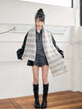 Full body shot of a young person wearing a light grey and pink striped knit scarf, black jacket, and boots.