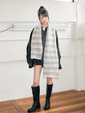 A young person showcases a long, striped knit scarf in light grey and pink hues.