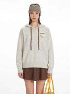 Front view of a woman in a speckled knit hoodie, showcasing the drawstring and pocket detail.