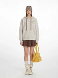 Model wearing a light grey flecked knit hoodie with a brown pleated mini skirt and cream boots.