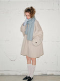 Full body shot of a woman wearing a light blue scarf, beige jacket, white socks, and black loafers.