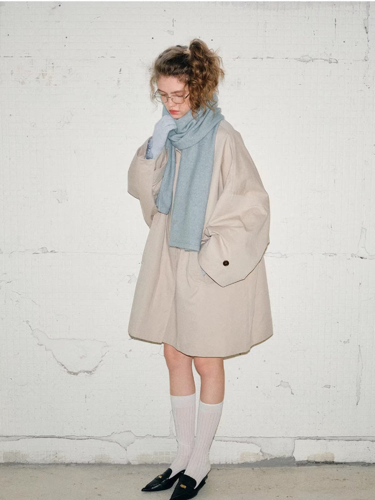Full body shot of a woman wearing a light blue scarf, beige jacket, white socks, and black loafers.