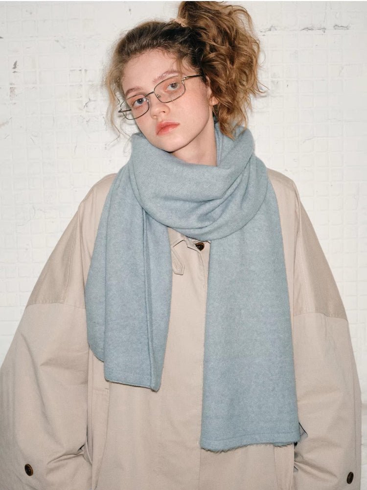 Woman wearing a light blue knit scarf draped around her neck, over a beige jacket.