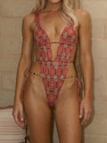 Woman wearing a red and grey printed one-piece swimsuit with a deep V-neck and high-cut legs.