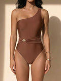 Woman wearing a brown one-shoulder one-piece swimsuit with a removable belt featuring a gold shell buckle.