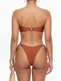 Back view of a woman in a rust-colored bikini, showing the adjustable side ties and a gold clasp closure on the top.