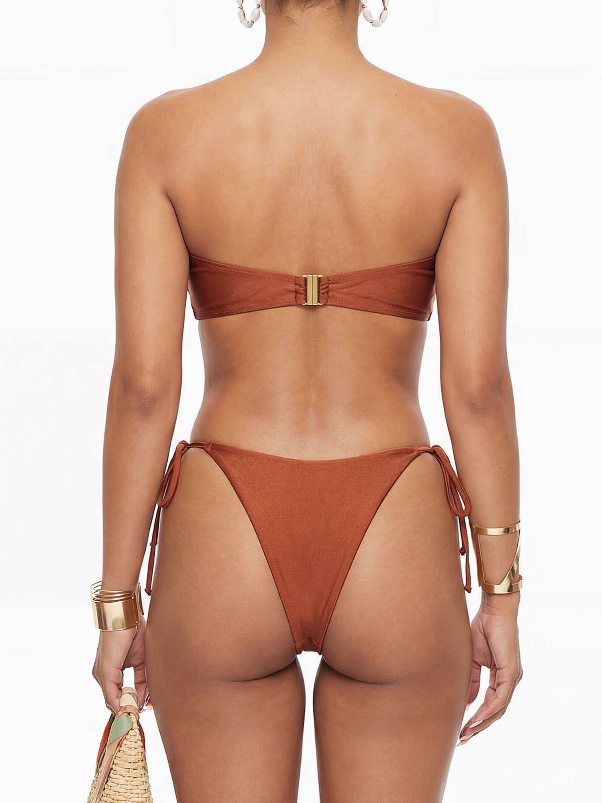 Back view of a woman in a rust-colored bikini, showing the adjustable side ties and a gold clasp closure on the top.