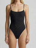 Woman wearing a black one-piece swimsuit with all-over white polka dots and rhinestone embellishments