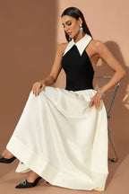 Woman in a black halter top dress with a white pointed collar and a full ivory skirt, sitting on a chair.