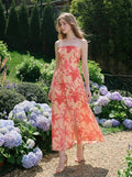 Woman wearing a strapless peach maxi dress with a red floral print and a side slit, walking in a garden with hydrangeas.