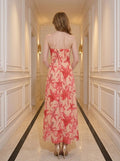 Back view of a woman in a strapless peach maxi dress with a red floral print, standing in a hallway.