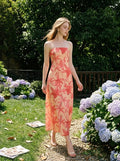 Woman wearing a strapless peach maxi dress with a red floral print, walking in a garden with hydrangeas.