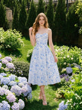 Woman wearing a blue and white floral print midi dress with spaghetti straps, posing in a garden with hydrangeas.