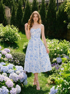 Woman wearing a blue and white floral print midi dress with spaghetti straps, posing in a garden with hydrangeas.