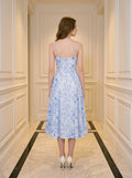 Back view of a woman in a blue and white floral print midi dress with spaghetti straps, standing in a hallway.