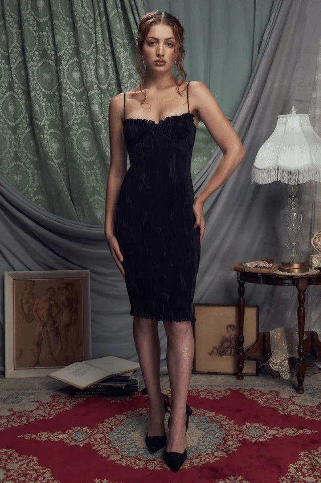 Woman wearing a black ruched sheath dress with spaghetti straps and scalloped trim.