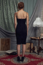 Back view of a woman in a black ruched sheath dress with spaghetti straps.