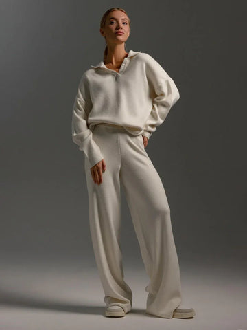 Woman wearing a cream knit loungewear set with a collared sweater and wide-leg pants, posing against a grey background.