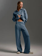 Woman wearing a blue knit loungewear set with a collared sweater and wide-leg pants, standing against a grey background.
