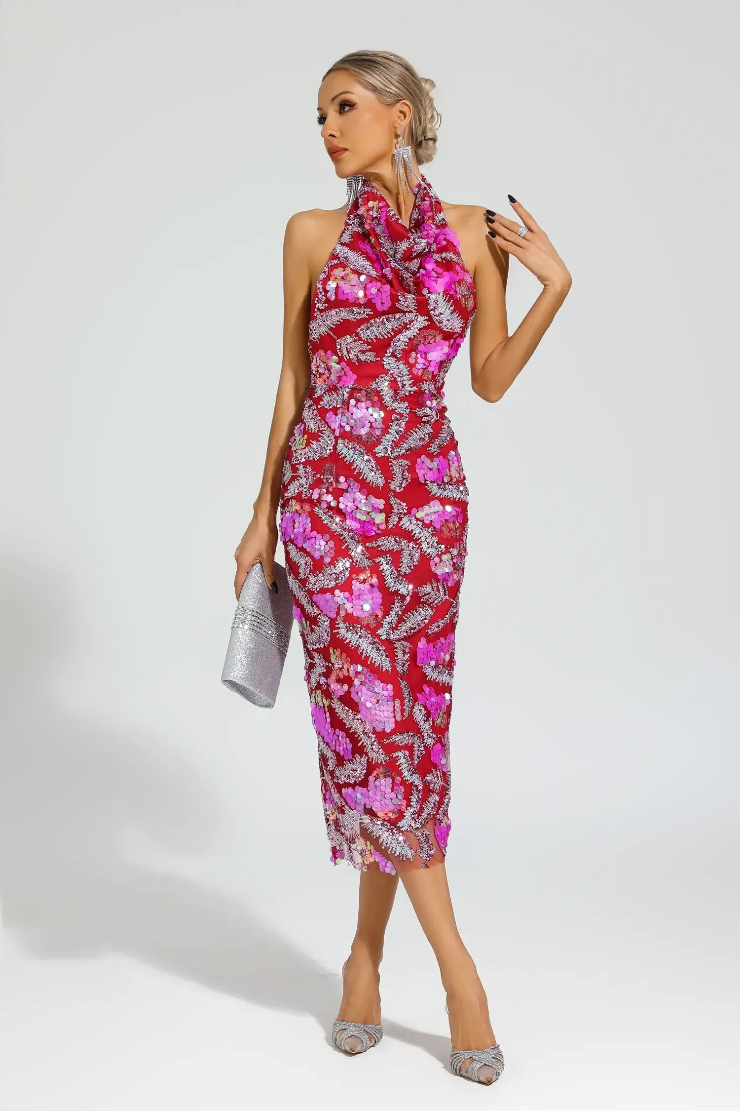 A model wearing a pink and red floral halter midi dress with sequin appliques, paired with silver accessories and shoes.