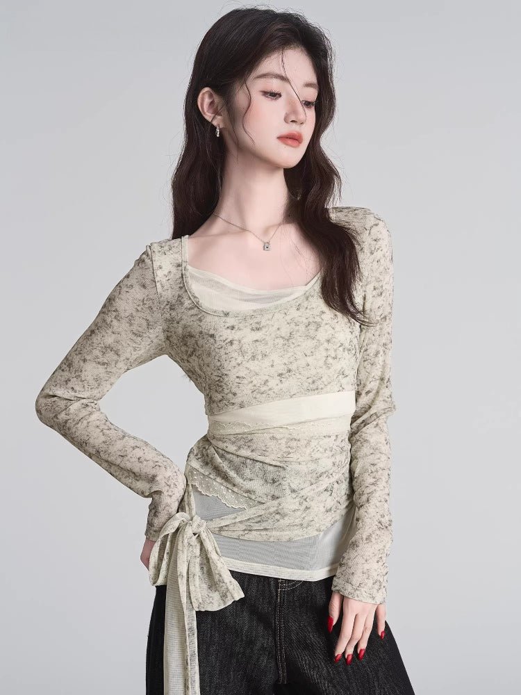 Woman wearing a light-colored, long-sleeved sheer mesh top with a floral-like print and a tie detail at the waist.