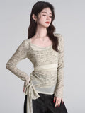 Front view of a woman in a layered long-sleeve top featuring a square neckline and a decorative waist tie.