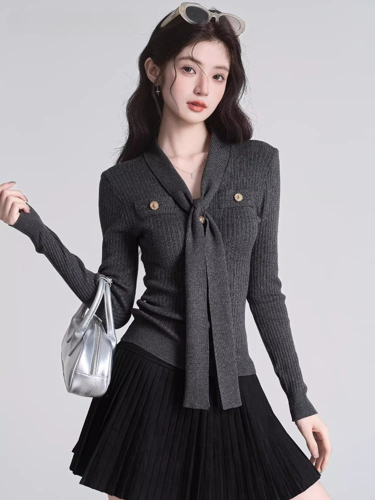 Woman wearing a dark grey ribbed knit long-sleeve top with a tie-neck and gold buttons.