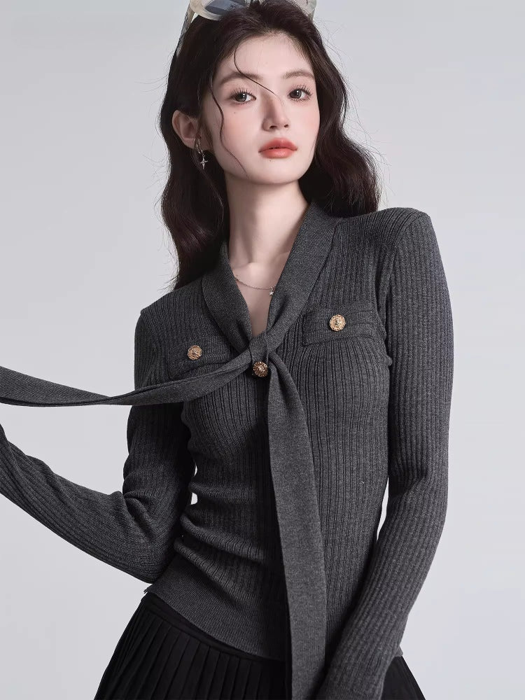 Close-up of a dark grey ribbed knit top featuring a tie-neck and decorative gold buttons.