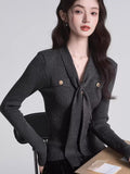 Woman wearing a dark grey ribbed knit long-sleeve top with a tie-neck and gold buttons.