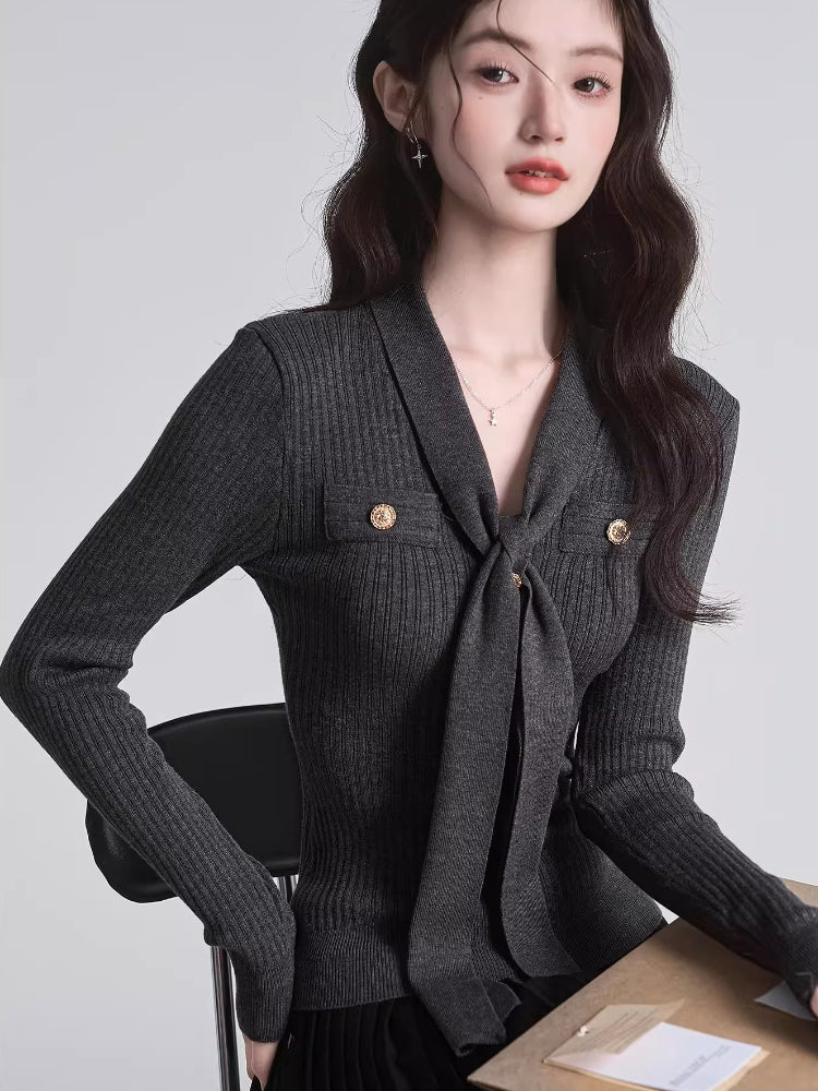 Woman wearing a dark grey ribbed knit long-sleeve top with a tie-neck and gold buttons.