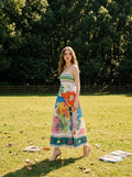 Woman standing in a grassy field wearing a sleeveless midi dress with a bright abstract tropical design.
