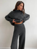 Woman wearing a charcoal knit turtleneck sweater and wide leg pants, adjusting sweater