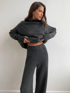 Woman wearing a charcoal knit turtleneck sweater and wide leg pants, adjusting sweater