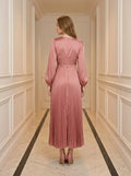 Back view of a woman in a pink satin midi dress with a twisted knot bodice and pleated skirt.