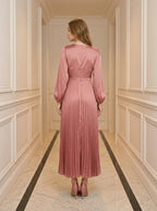 Back view of a woman in a pink satin midi dress with a twisted knot bodice and pleated skirt.