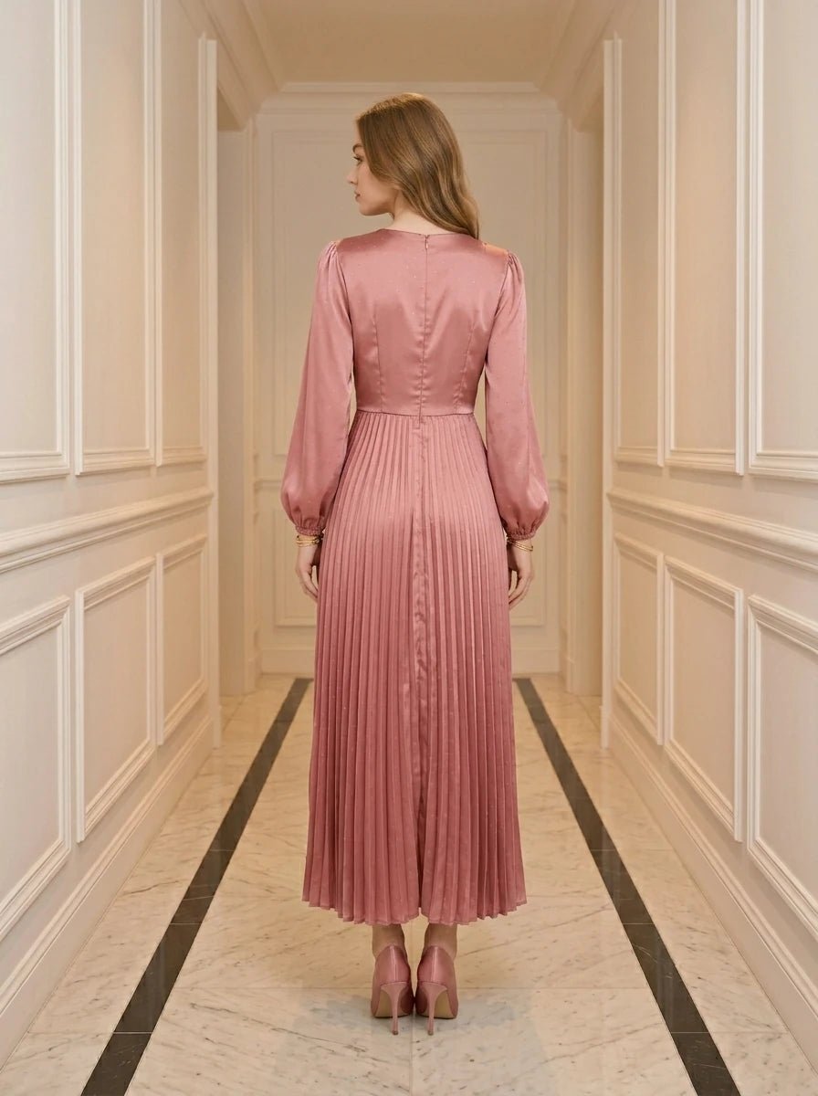 Back view of a woman in a pink satin midi dress with a twisted knot bodice and pleated skirt.
