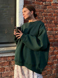 Woman wearing a dark green oversized sweatshirt and floral skirt holding a coffee cup.