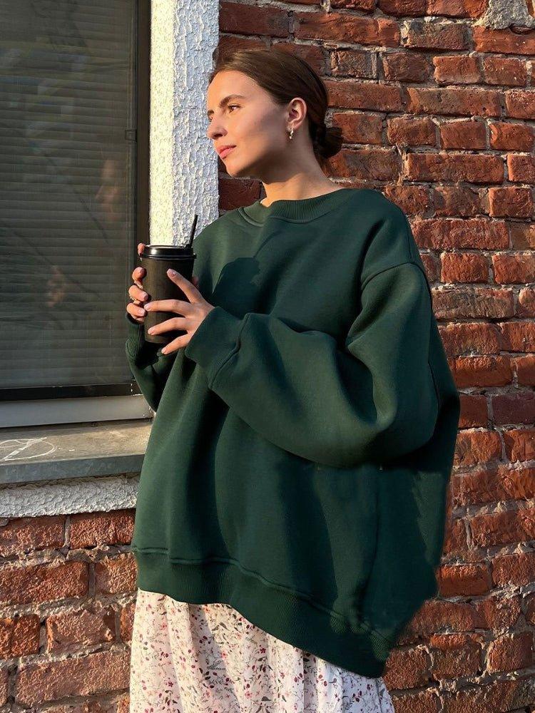 Woman wearing a dark green oversized sweatshirt and floral skirt holding a coffee cup.
