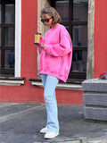 Woman in a pink oversized sweatshirt and jeans holding a coffee cup and phone.