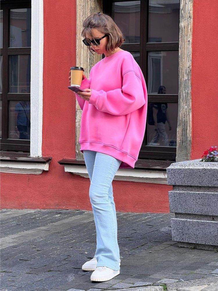 Woman in a pink oversized sweatshirt and jeans holding a coffee cup and phone.
