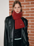 Woman wearing a red knit scarf with a ribbed texture and a small gold brand tag.