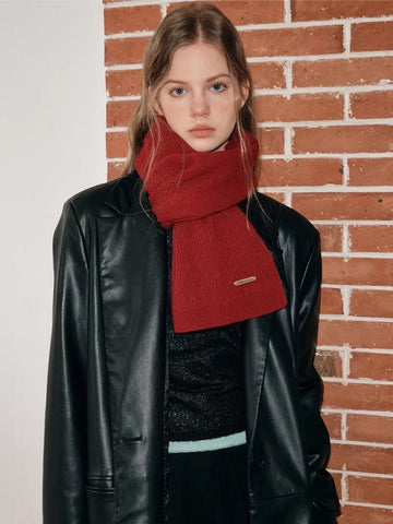 Woman wearing a red knit scarf with a ribbed texture and a small gold brand tag.