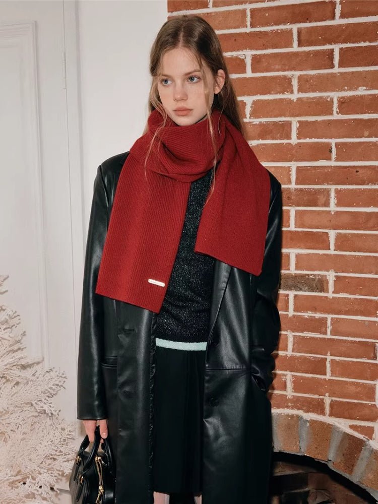 A woman poses in a red ribbed scarf, layered with a black coat.