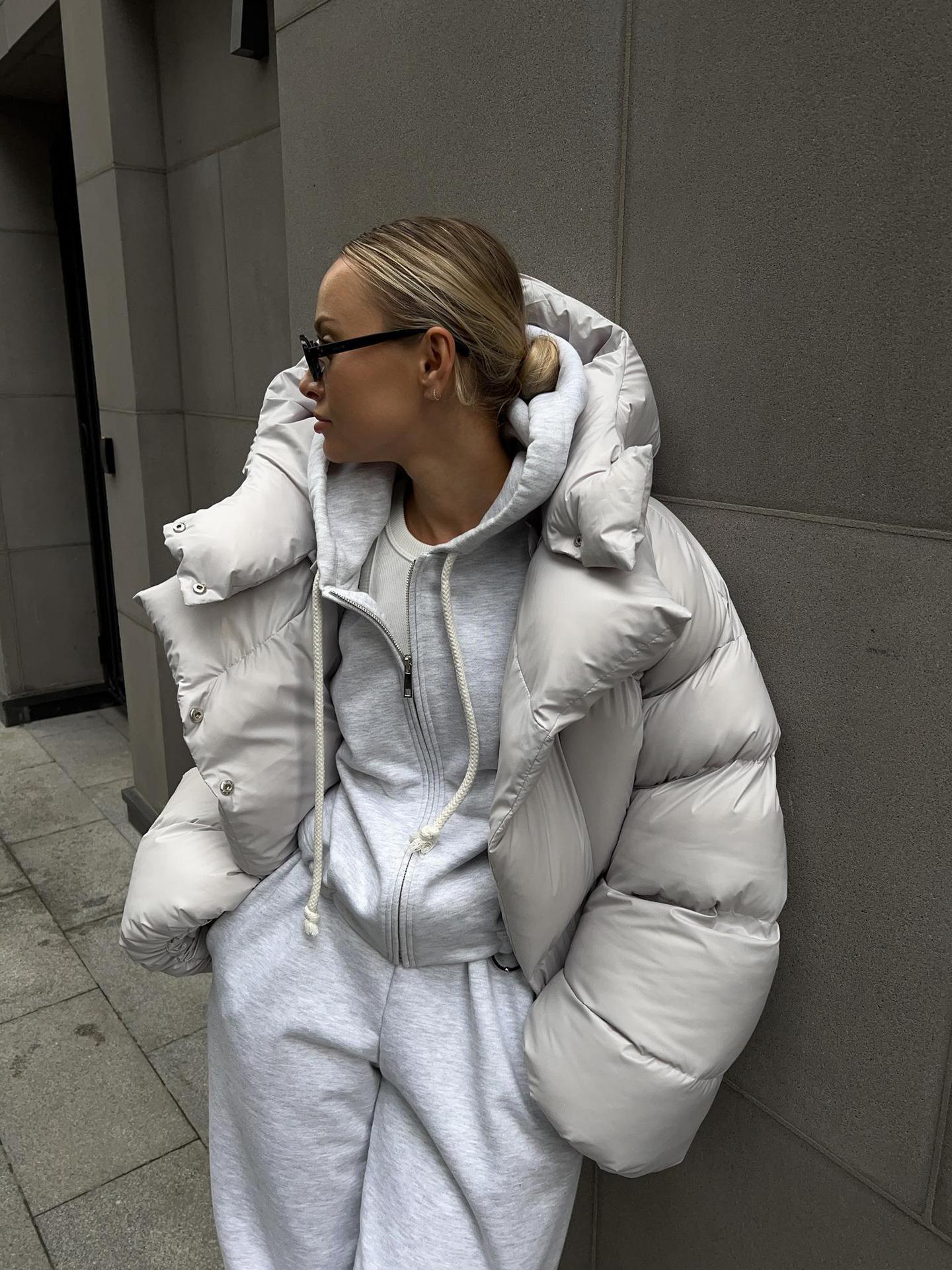 Side profile of a woman wearing a light grey hooded puffer jacket.